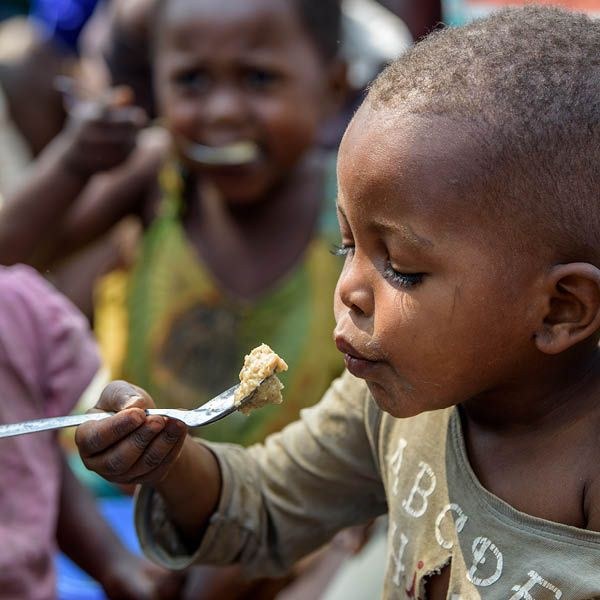 A young child eating from a fork, surrounded by other children at mealtime