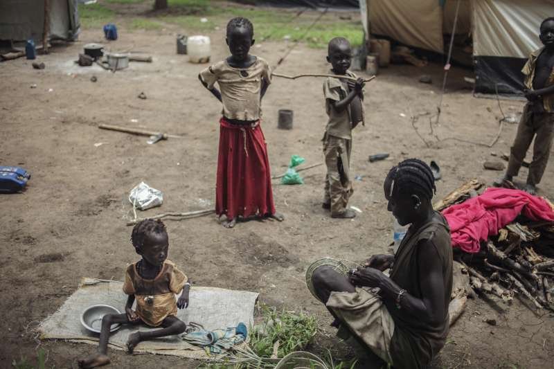 Children and a woman at a temporary camp, with water containers and cooking pots on the ground